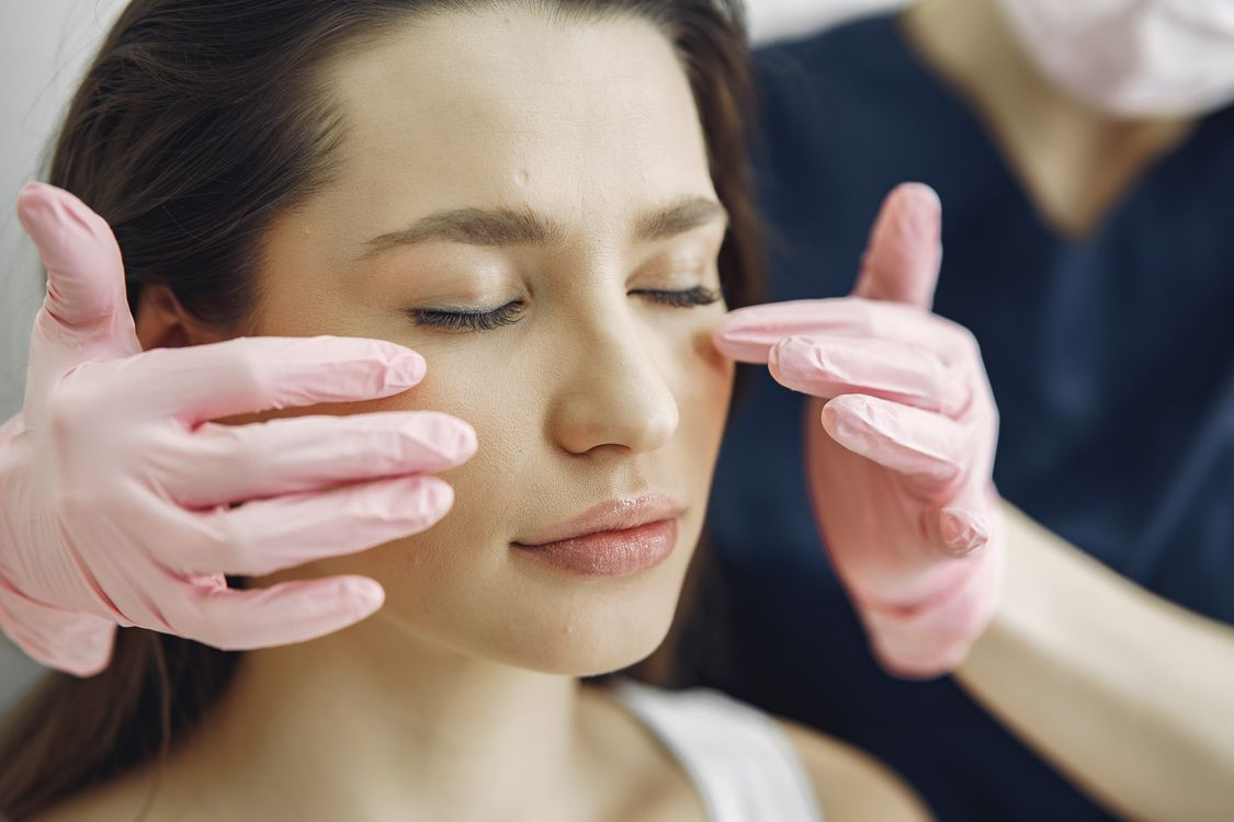 Woman relaxing during a facial treatment as a clinician with pink gloves holds her face gently with hands on cheeks and temples